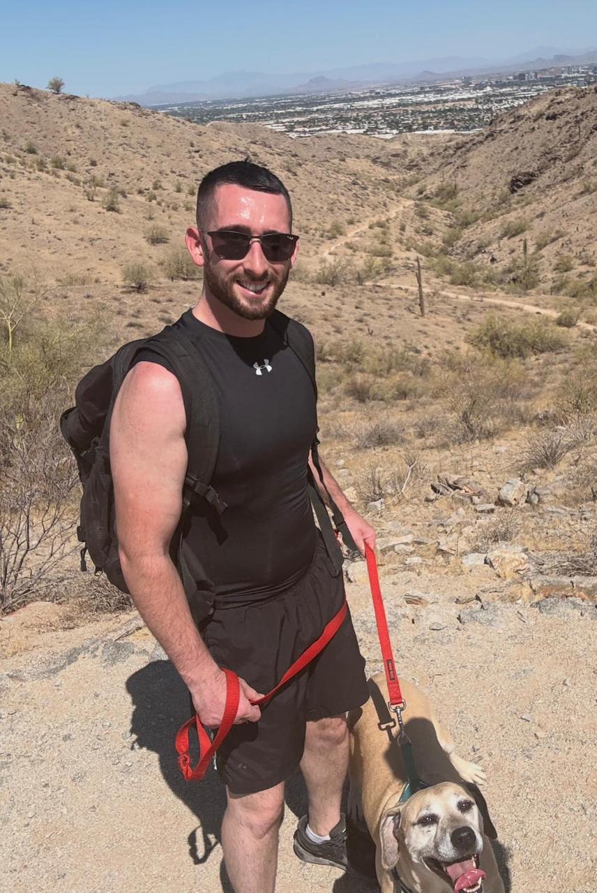 Tyler Guertin standing with a dog on a desert trail.